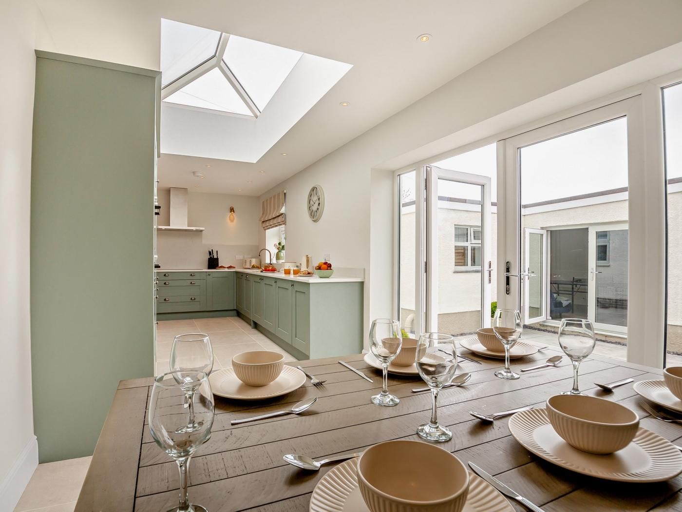 A modern kitchen with a skylight, a dining area with a table set for four, and a view through large sliding glass doors.