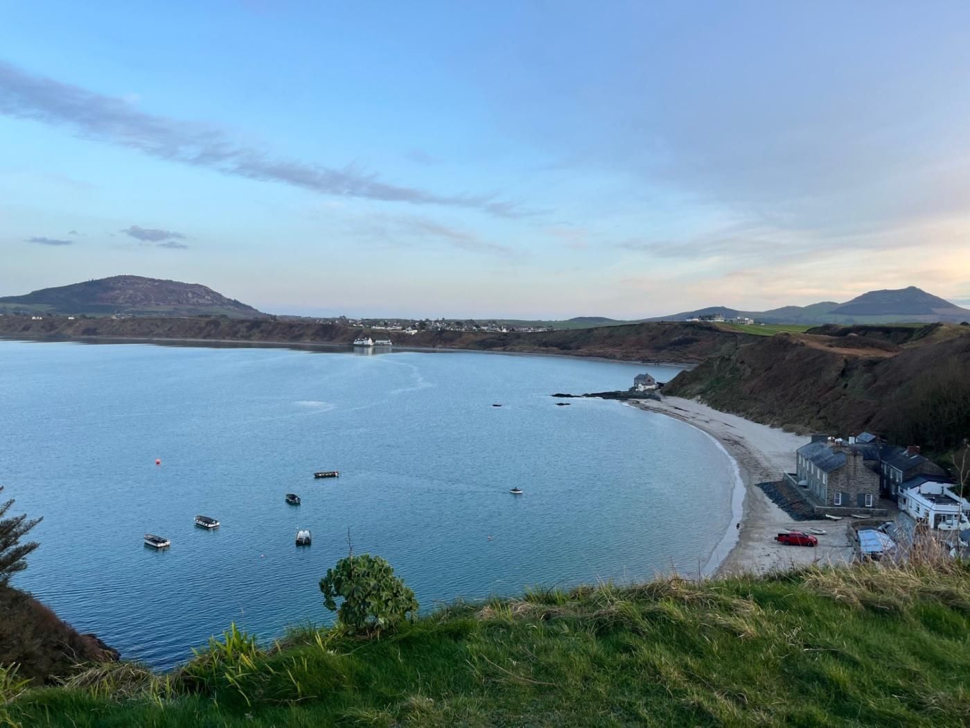 Un paysage côtier avec un ciel dégagé, une mer calme et une petite plage bordée de bâtiments.