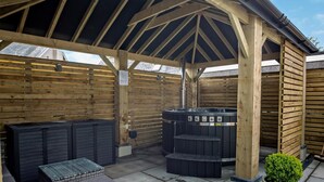 Ein überdachter Außenbereich mit Whirlpool, Sitzgelegenheiten und einer Holzkonstruktion.