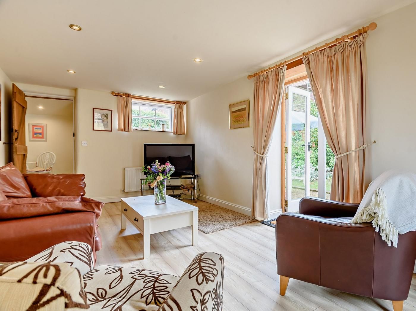 A living room with a sofa, armchair, coffee table, TV, and a window with curtains.