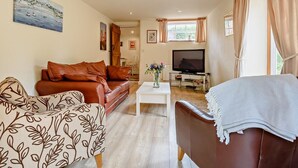Een woonkamer met een bruine leren bank, een fauteuil met een patroon, een salontafel en een televisie.