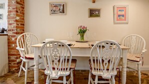Een eetruimte met een houten tafel, vier witte stoelen en een bloevas. Drie ingelijste foto's hangen aan de muur.