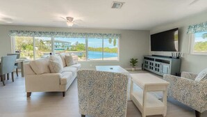 Una sala de estar con sofá, sillones, una mesa de centro, televisor y vista a una piscina.