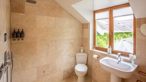 Ein Badezimmer mit Dusche, Toilette und Waschbecken, mit Oberlicht und Blick auf Grünflächen.