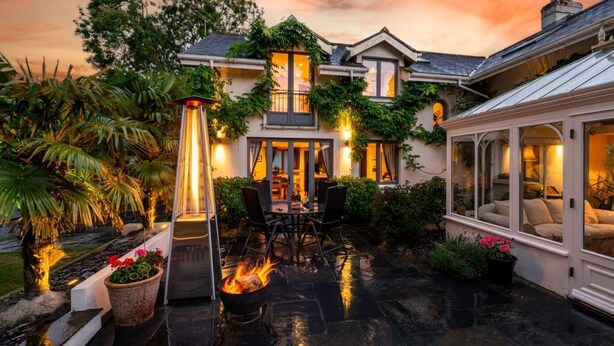Ein Haus mit Terrasse, Feuerstelle und Wintergarten.