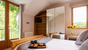 Ein Schlafzimmer mit einem großen Bett, einem Holfnachtkästchen, einem kleinen Nachttisch mit einer Vase voller Sonnenblumen, einem Heizkörper und einem Fenster mit Balkonblick.