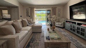 Ein Wohnzimmer mit Sofa, Couchtisch, Fernseher und Blick auf einen Pool.