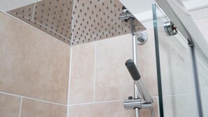 Eine Dusche mit einer Lochplatte an der Decke, einer Handbrause und einer Glasduschwand.