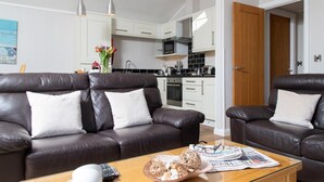 Ein modernes Wohnzimmer mit zwei Ledersofas, einem Glastisch und einer Küche im Hintergrund.