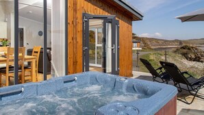 Ein modernes Holzgebäude mit Glastür, die zu einem Essbereich und einem Whirlpool führt.