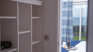 Une chambre à coucher avec un lit, une fenêtre avec des rideaux, une vue sur la mer et une armoire avec des étagères.