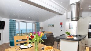 Een moderne keuken met een gasfornuis, een eethoek met een houten tafel en uitzicht op zee door grote ramen.
