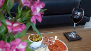 Een bord met kaas, olijven, parmaham en salami, een glas rode wijn en een vaas met roze bloemen op een houten tafel.