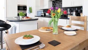 Een moderne keuken met witte kastjes, een zwart aanrecht en een eettafel met borden eten en een vaas tulpen.
