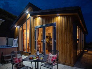 Une cabane en bois comprenant un coin repas, un jacuzzi et une cuisine visible à travers les portes vitrées.