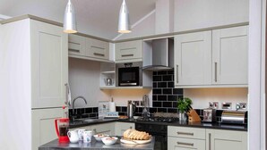 A modern kitchen with white cabinets, a black backsplash, stainless steel appliances, and a central island with seating. - 1 Bed in Castle Douglas (oc-rasc2) (Auchencairn)