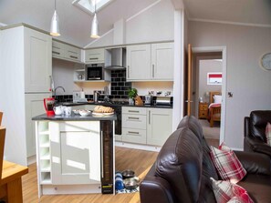 A modern kitchen with white cabinets, a central island, and a dining area with a brown leather sofa. - 1 Bed in Castle Douglas (oc-rasc2) (Auchencairn)
