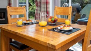 A wooden dining table with breakfast items, a pitcher of orange juice, and a fruit bowl. - 1 Bed in Castle Douglas (oc-rasc2) (Auchencairn)