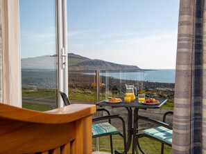 Ein Balkon mit Frühstückstisch, der auf eine Küstenlandschaft mit Hügeln und einem Gewässer blickt.