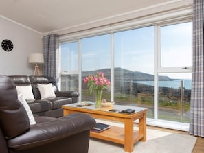 Ein modernes Wohnzimmer mit einer Ledersofa, einem Glastisch und Meerblick durch große Fenster.