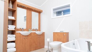Un baño moderno con tocador de madera, dos lavamanos, inodoro y bañera.