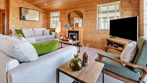 Een knus blokhutinterieur met een bank, fauteuil, televisie, open haard en houten wanden.