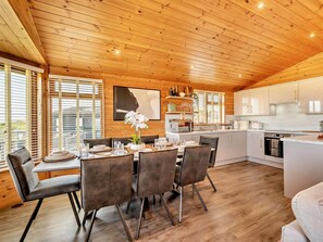 A modern kitchen with white cabinets, a central island, and a dining area with a table set for four. - 3 Bed in Ilfracombe (oc-95047) (Ilfracombe)