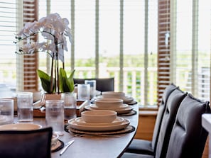 A dining table set with plates, bowls, and glasses, with a view of the outdoors through large windows. - 3 Bed in Ilfracombe (oc-95047) (Ilfracombe)