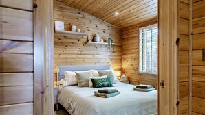 Een knus slaapkamer met een bed, nachtkastje, raam met zonwering en houten lambrisering.