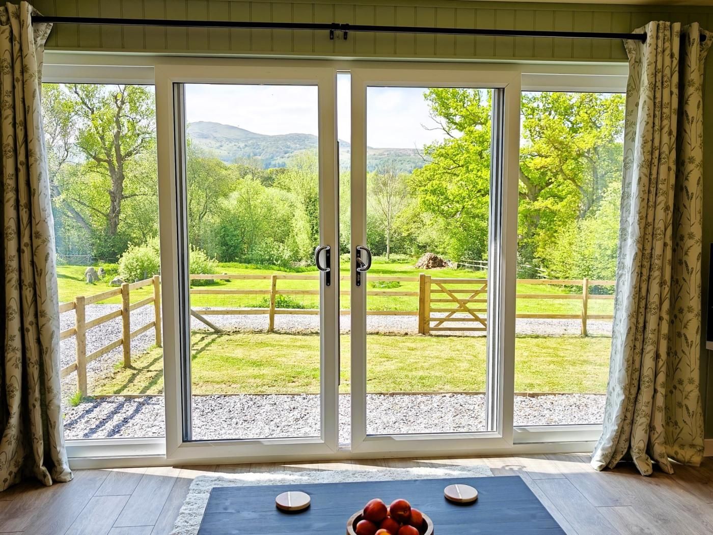 A room with a large sliding glass door leading to a grassy outdoor area with a wooden fence and a view of trees and hills.