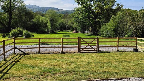A fenced outdoor area with a gravel path, surrounded by greenery and trees. - 1 Bed in Conwy (oc-95098) (Ty'n-y-groes)