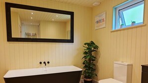 A bathroom with a freestanding bathtub, a toilet, a potted plant, a mirror, and a window. - 1 Bed in Conwy (oc-95098) (Ty'n-y-groes)