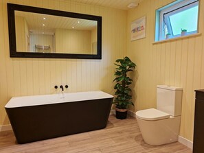 A bathroom with a freestanding bathtub, a toilet, a potted plant, a mirror, and a window. - 1 Bed in Conwy (oc-95098) (Ty'n-y-groes)