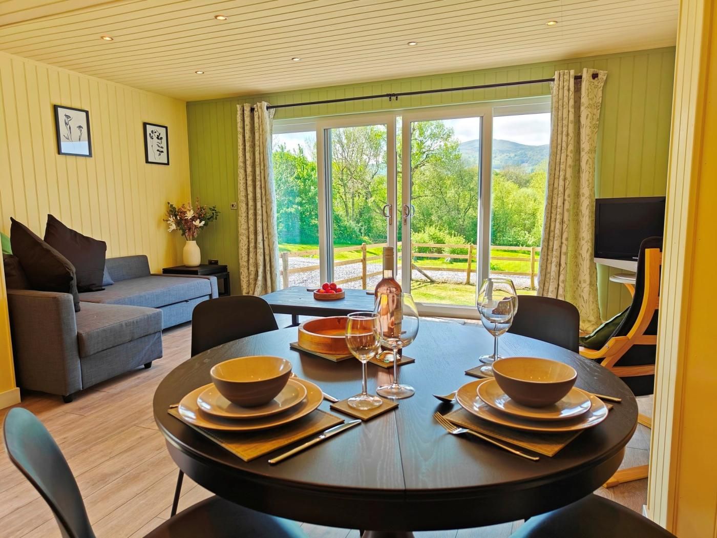 A dining area with a table set for four, a sofa, and a view of a green landscape.