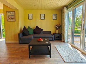 Habitació amb un sofà, una taula de centre amb fruita, obres d'art emmarcades a la paret i vistes a través de grans finestres.