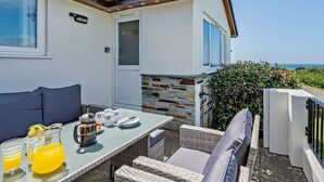 Eine Terrasse mit einem für das Frühstück gedeckten Tisch, Sitzgelegenheiten im Freien und Blick aufs Meer.