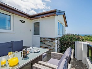 Eine Terrasse mit einem für das Frühstück gedeckten Tisch, Sitzgelegenheiten im Freien und Blick aufs Meer.