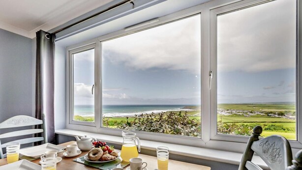 Ein Frühstückstisch mit Tellern, Gläsern und Blick auf das Meer durch große Fenster.