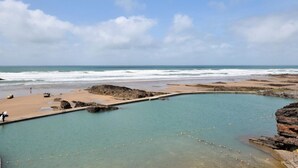 Eine Küstenlandschaft mit Schwimmbad, Strand und felsigem Gelände.