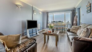 Ein Wohnzimmer mit Fernseher, Sofa, Couchtisch und einem Essbereich mit Tisch und Stühlen.