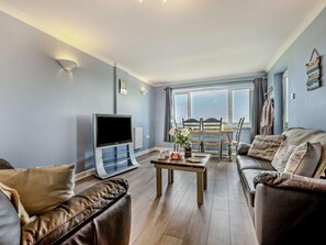 Ein Wohnzimmer mit Fernseher, Sofa, Couchtisch und einem Essbereich mit Tisch und Stühlen.