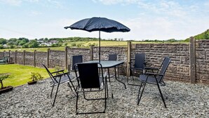 Eine Terrasse im Freien mit Tisch, Stühlen, einem schwarzen Sonnenschirm und einer Steinmauer.