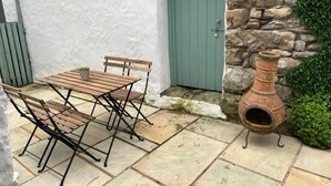 Un patio con una mesa y sillas de madera, un muro de piedra, una puerta verde y una maceta de barro.