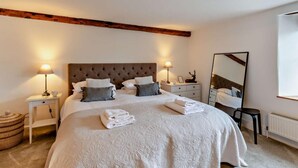 Un dormitorio con una cama grande, dos mesitas de noche, un espejo y un techo con vigas de madera.