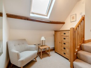 A room with a sloped ceiling, a skylight, a sofa, a small table with a lamp, a wooden cabinet, and a staircase. - 2 Bed in Chepstow (oc-95046) (Chepstow)