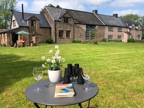 A stone building with a grassy lawn, a table with wine glasses, a book, and binoculars. - 2 Bed in Chepstow (oc-95046) (Chepstow)