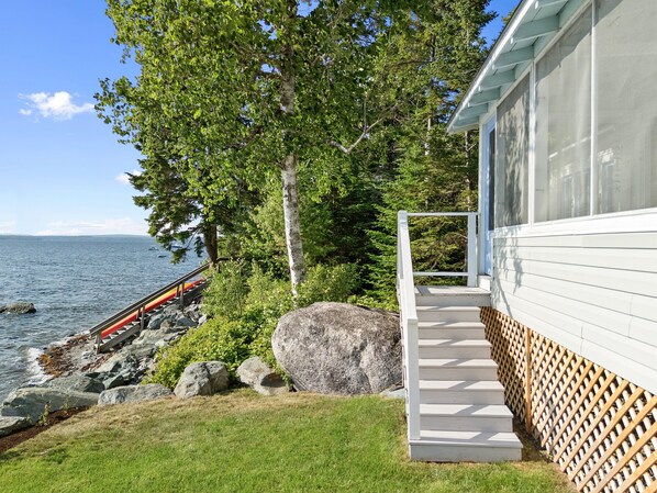 En fastighet vid kusten med en träterrass, en gång av sten och utsikt över havet.