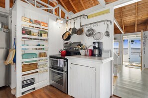 A kitchen with white cabinetry, a stove, and a coffee maker. - Sunset Cottage: Bayfront 3BR cottage with beach access, fire pit, WiFi, and Acadia nearby (Trenton)
