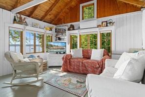 A cozy room with a wooden ceiling, a television, a bookshelf, and a view of the outdoors.