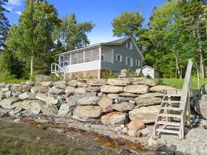 A house with a stone retaining wall, a wooden ladder, and a clear view of the water. - Sunset Cottage: Bayfront 3BR cottage with beach access, fire pit, WiFi, and Acadia nearby (Trenton)